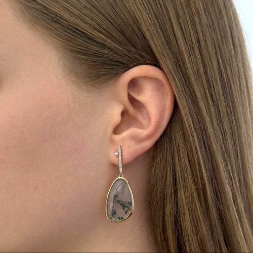 Woman wearing a gold earring with a teardrop-shaped gemstone in a store setting
