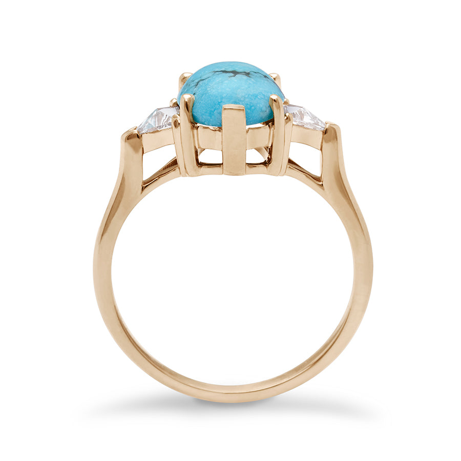 Side view of a three stone engagement ring with an opal shape turquoise center stone with two white diamond trillion side stones set in yellow gold.
