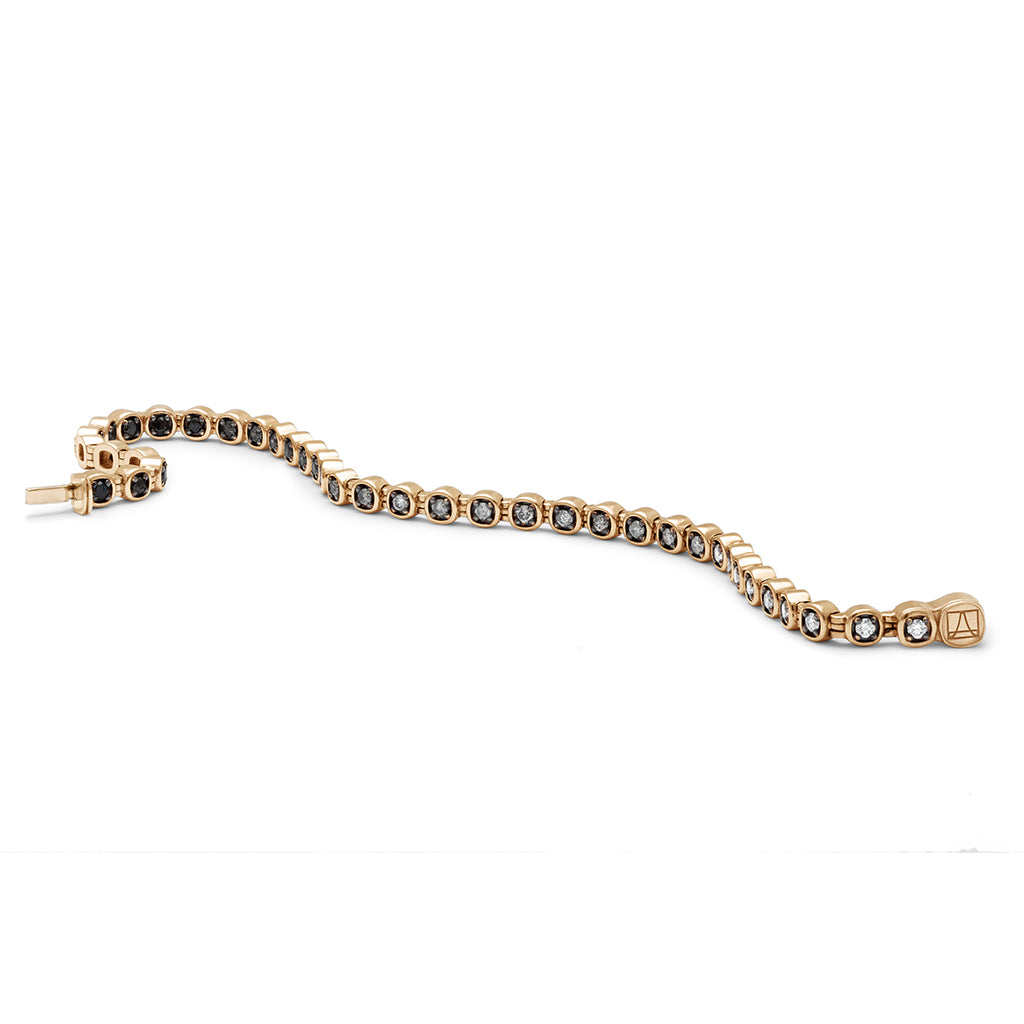 A styled view of a line bracelet with grey, white and black diamonds set in eternity with rhodium set in yellow gold.