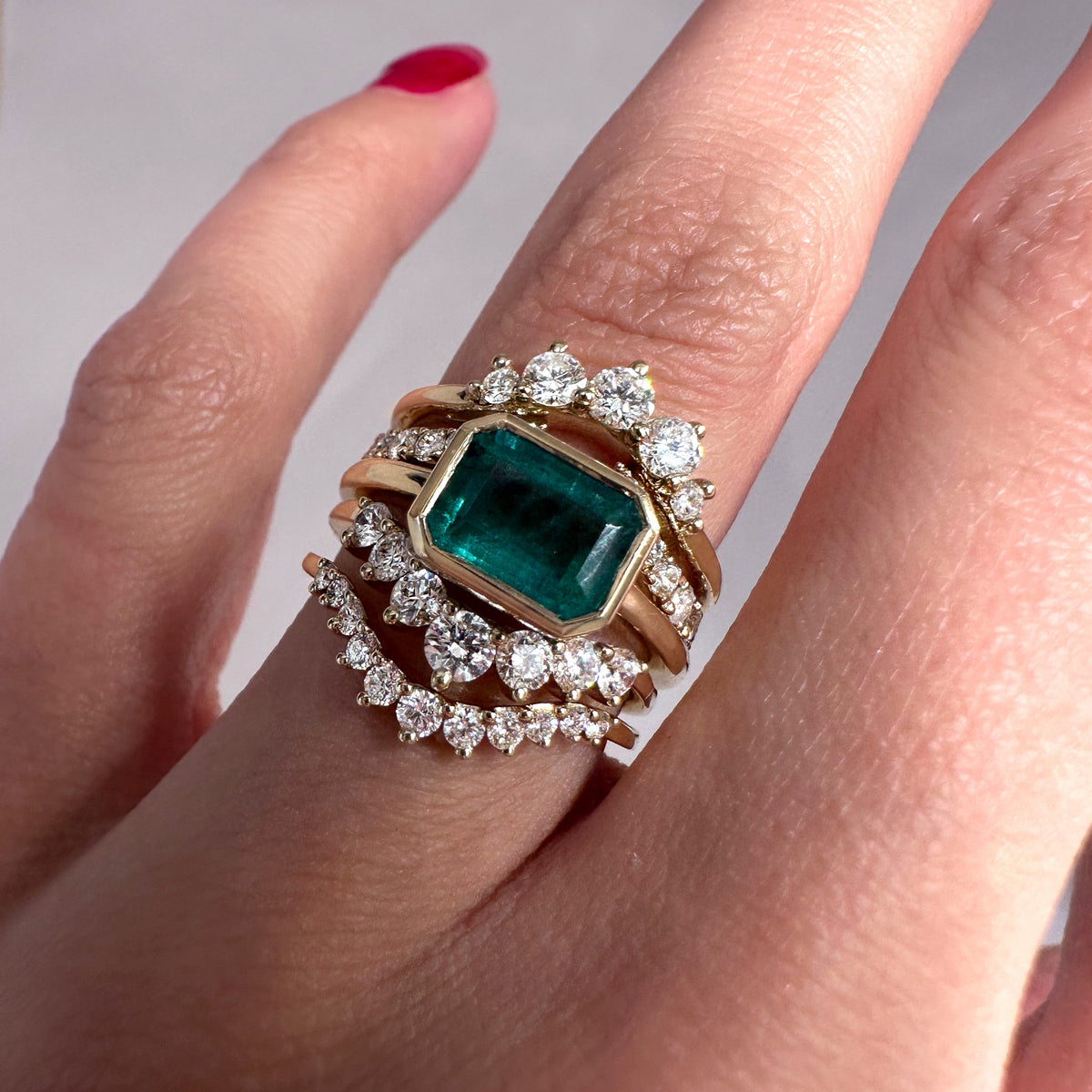 A close-up of a hand wearing a gold ring set with a large emerald-cut green gemstone and multiple rows of clear stones.