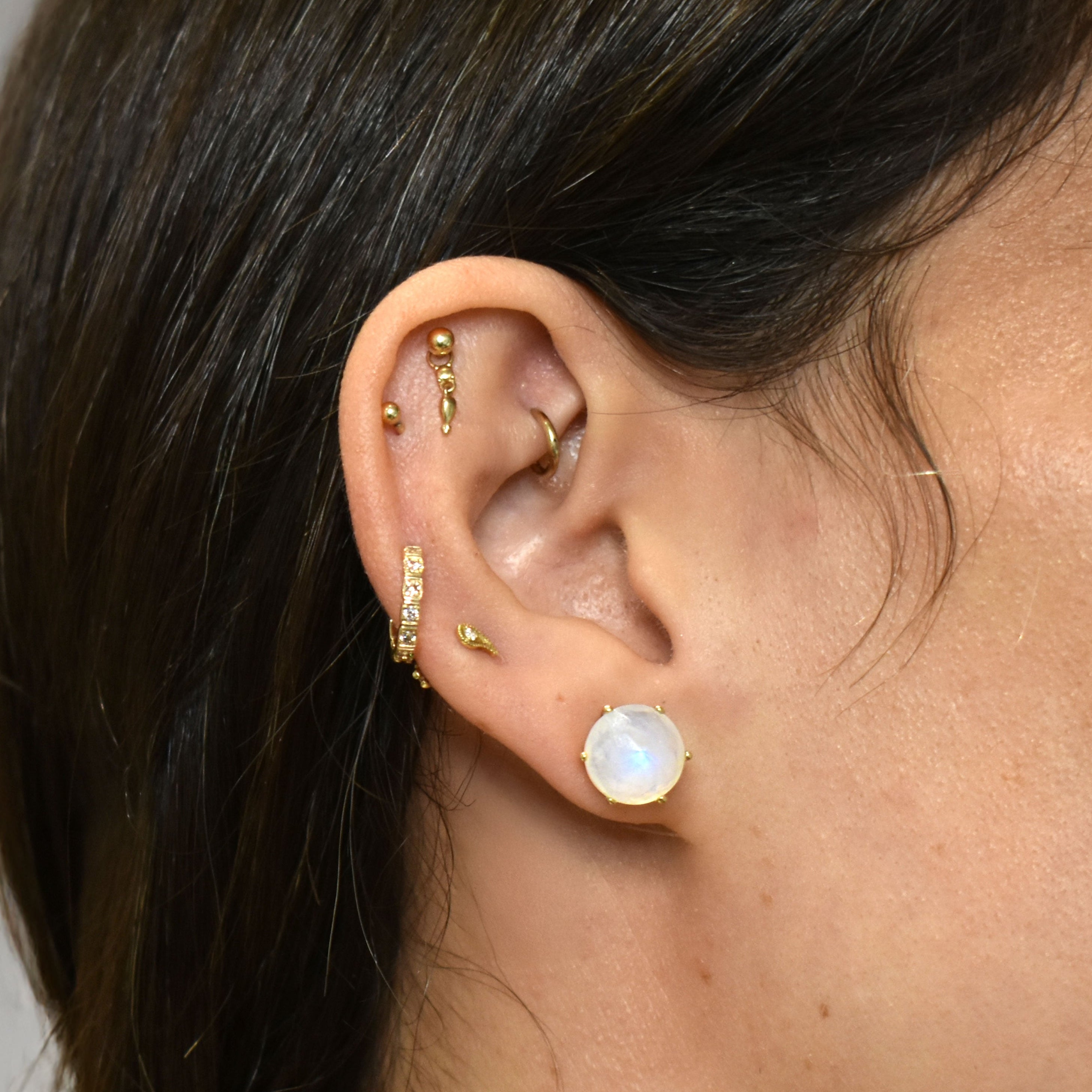 Close-up of an ear wearing gold earrings with a blurred background