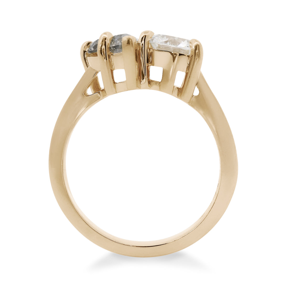 Two diamond toi et moi ring featuring a round brilliant white diamond and a pear shaped grey diamond with gold setting on a white background