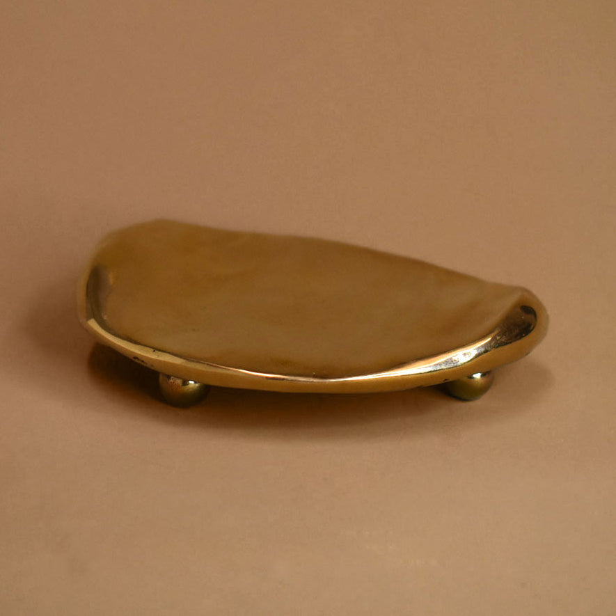 Flat, rippled, footed bronze dish on a beige background