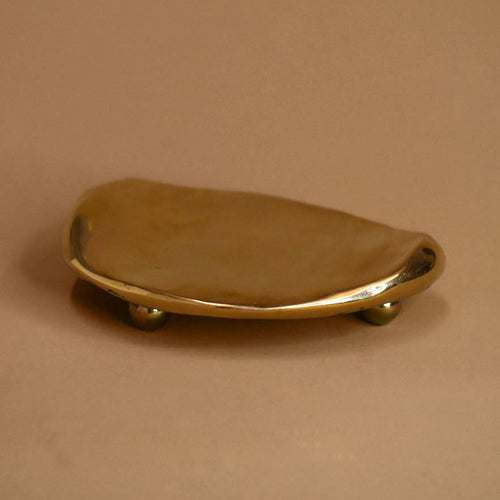 Flat, rippled, footed bronze dish on a beige background