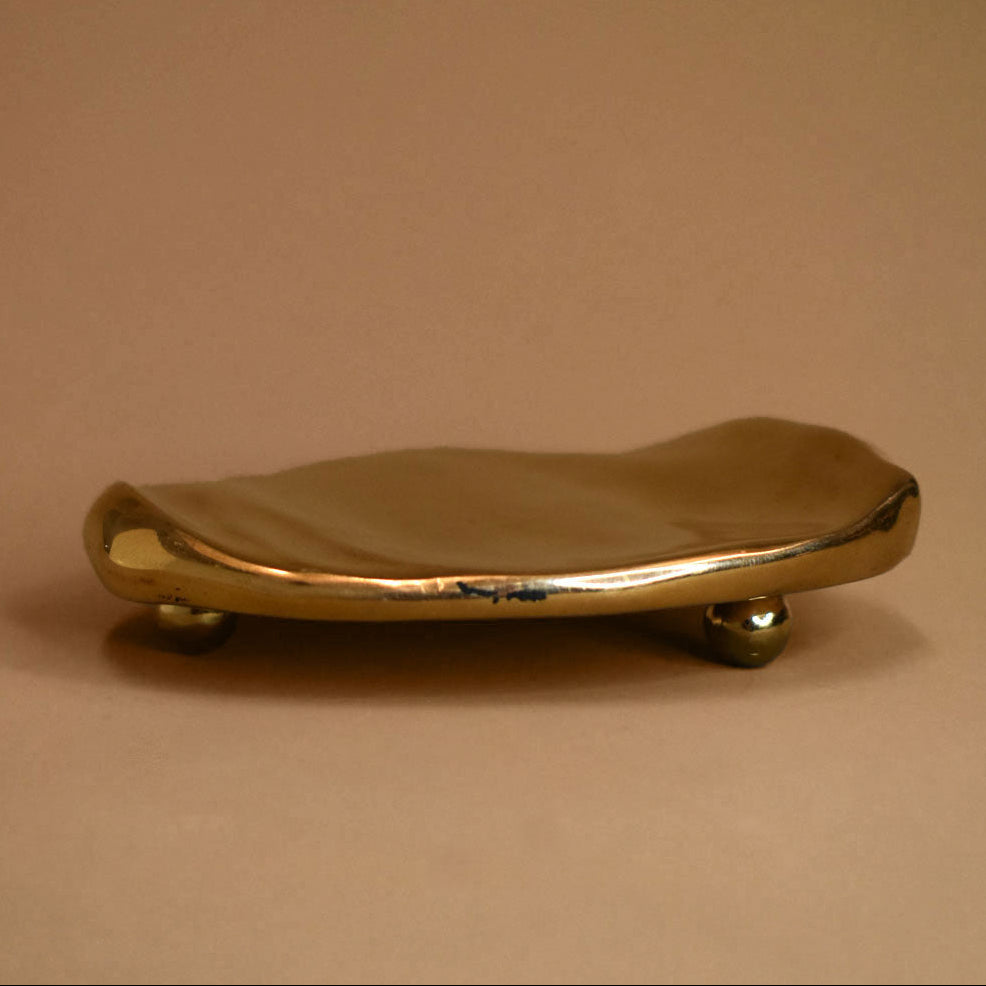 Flat, rippled, footed bronze dish on a beige background