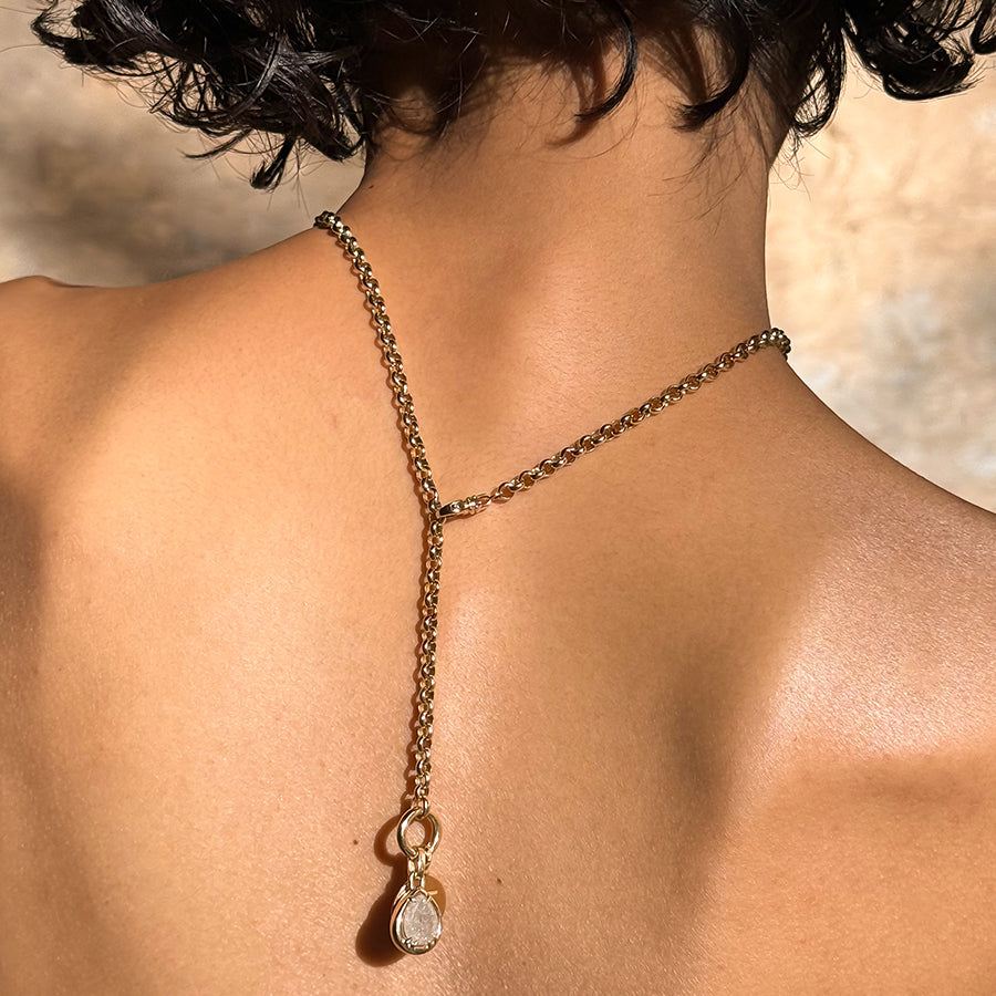 A medium-complexion model wears a rolo yellow gold chain with a grey diamond amulet charm at the bottom behind her back.