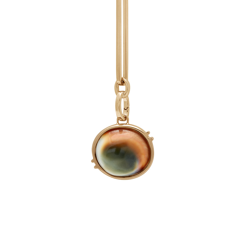A zoomed in view of a shiva stone charm in a bezel setting set in yellow gold on a mixed link yellow gold chain.