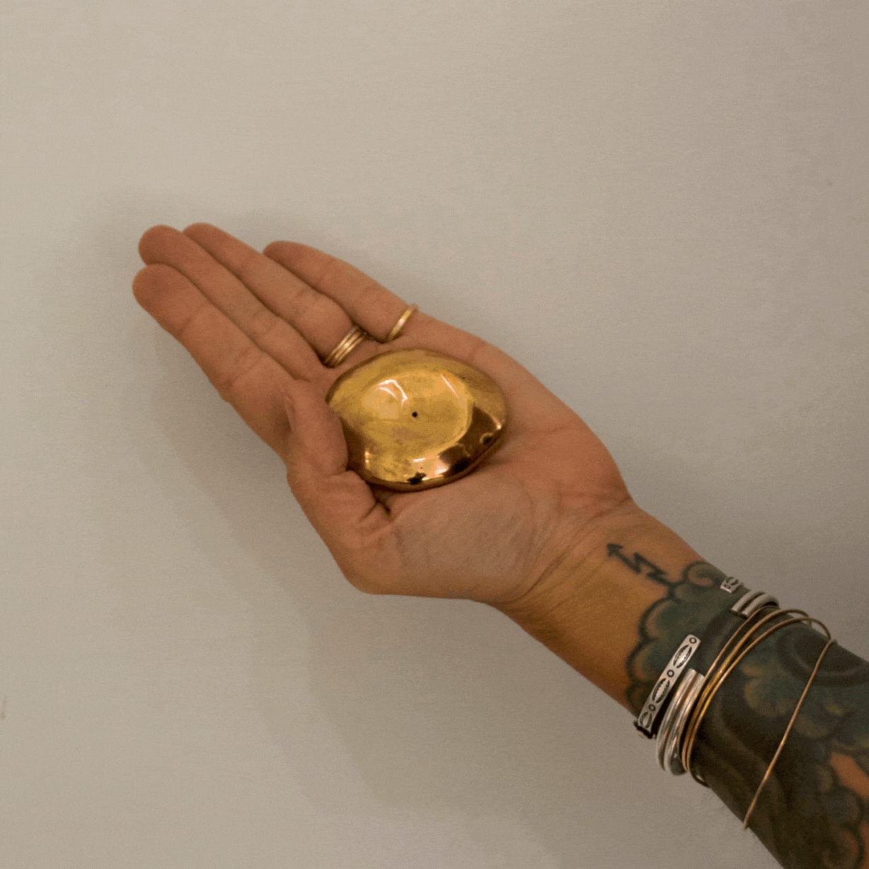 A gif of a hand holding a golden bronze small orb incense holder and tapping a blue incense stick into it against a white background 