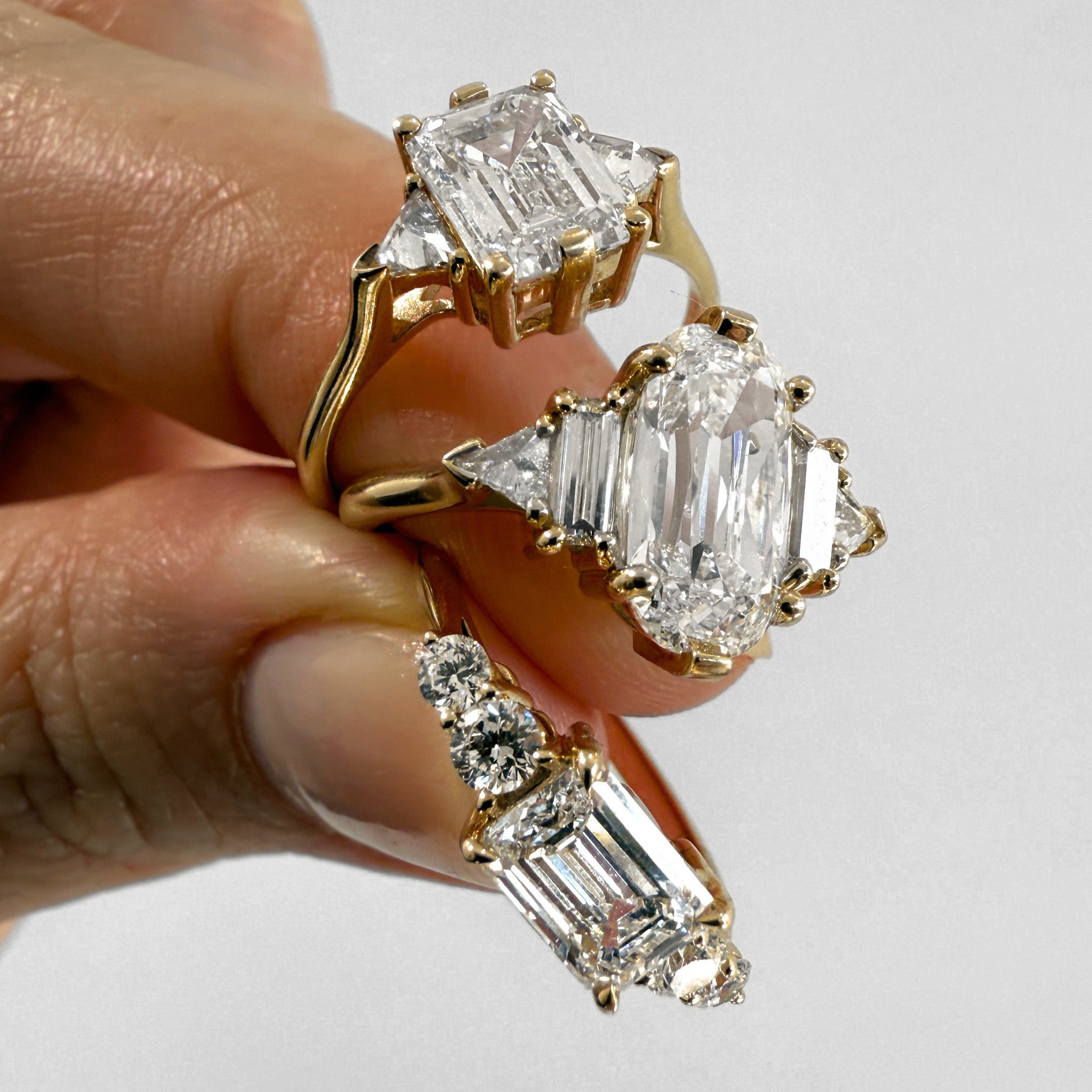 Gold and diamond earrings held by a hand against a light background