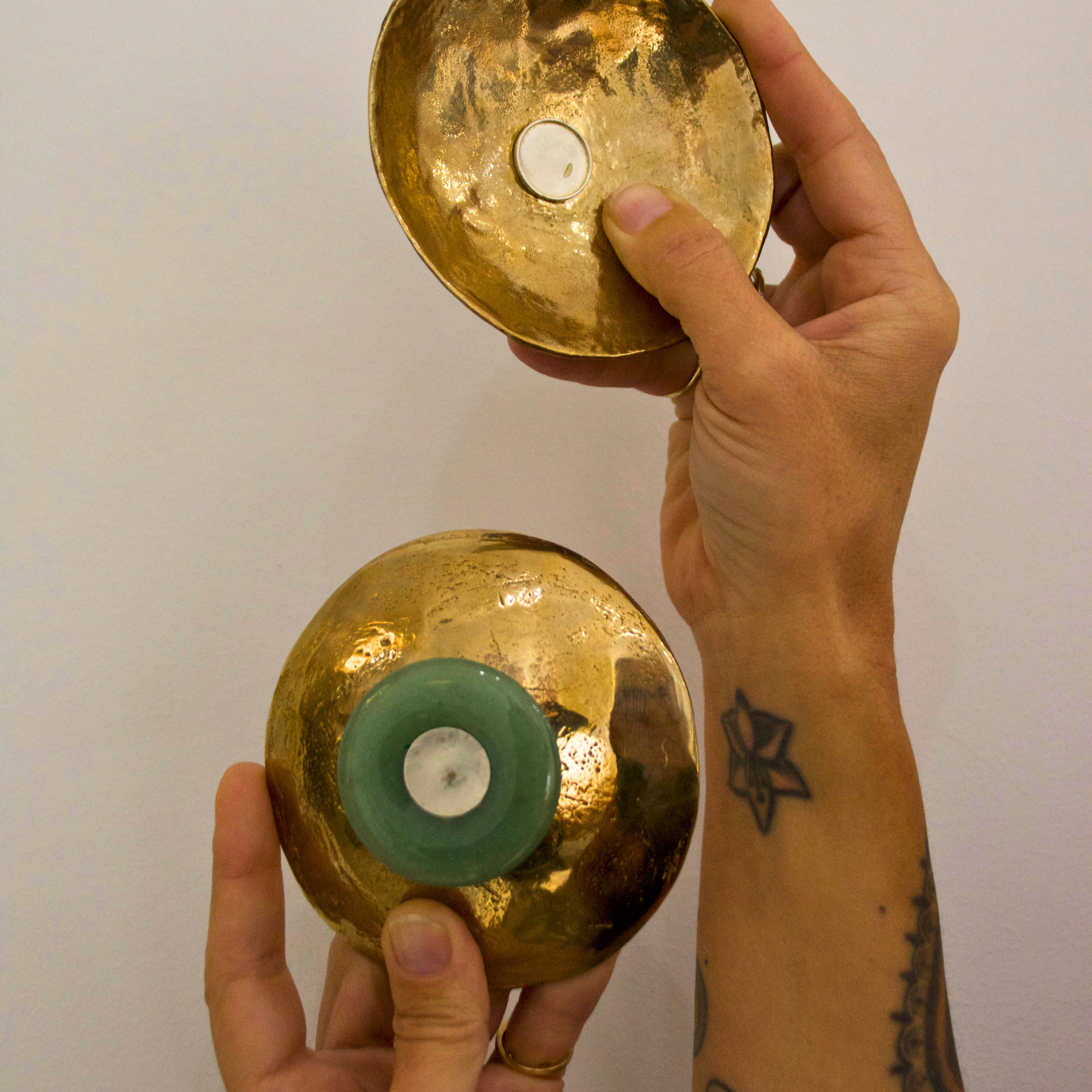 Two hands holding circular bronze dishes against a white background