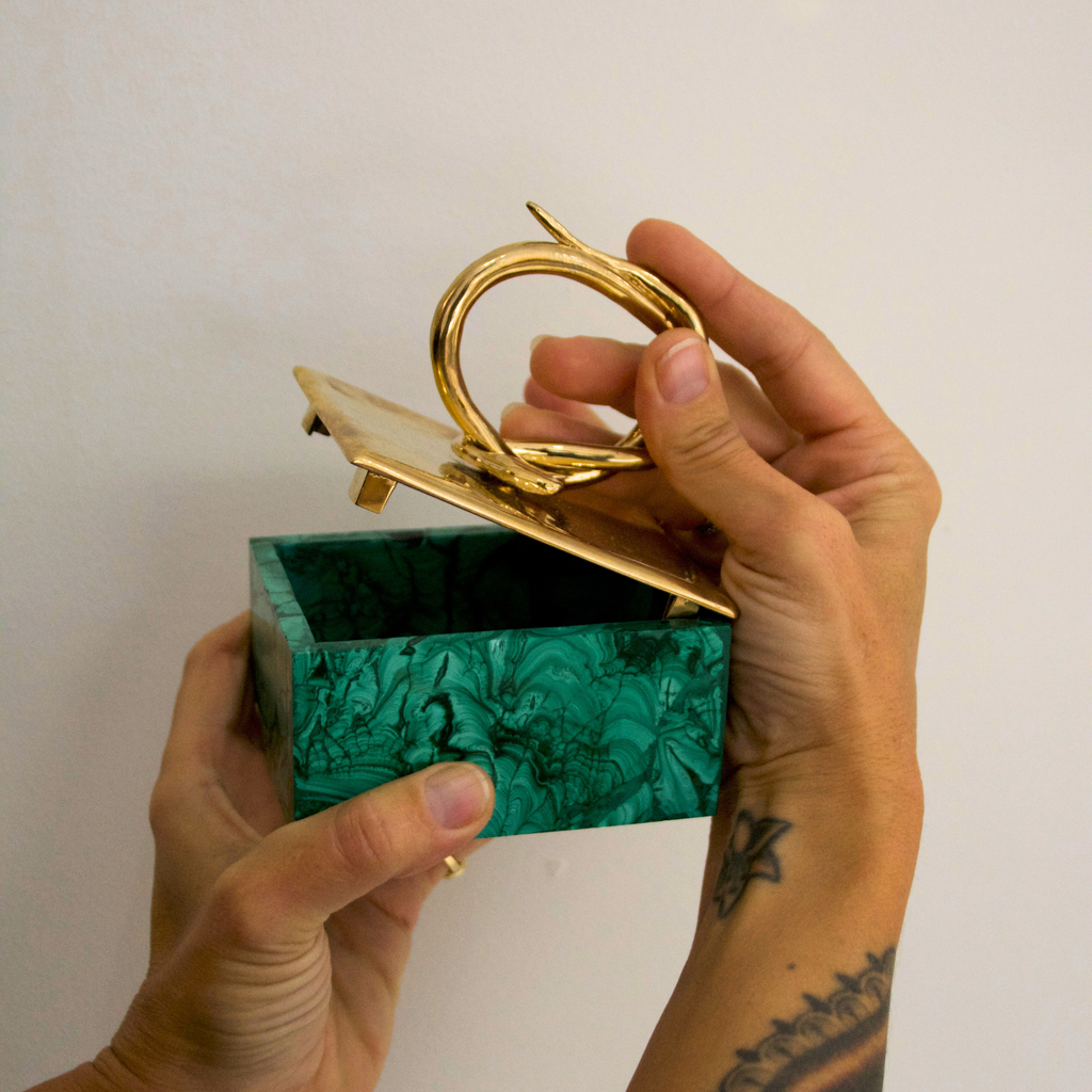 Hand holding a green marbled jewelry box with a gold lid against a white background
