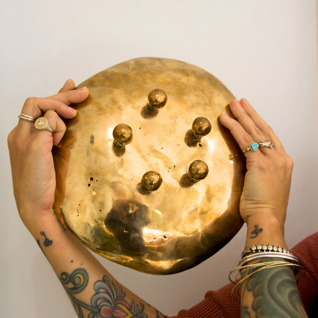 Two hands holding up the bottom of a  large bronze footed dish to expose the round feet against a white background
