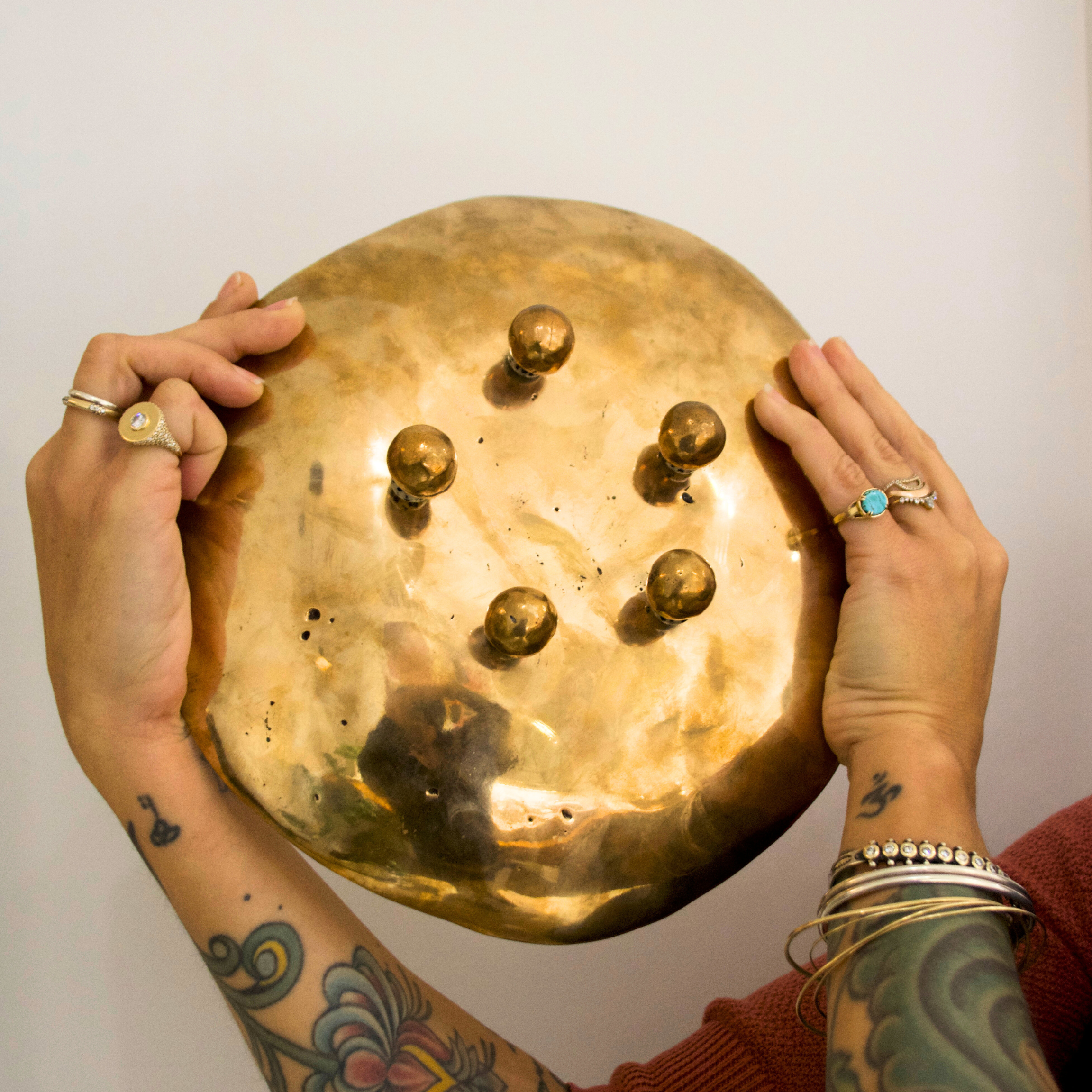 Two hands holding up the bottom of a  large bronze footed dish to expose the round feet against a white background