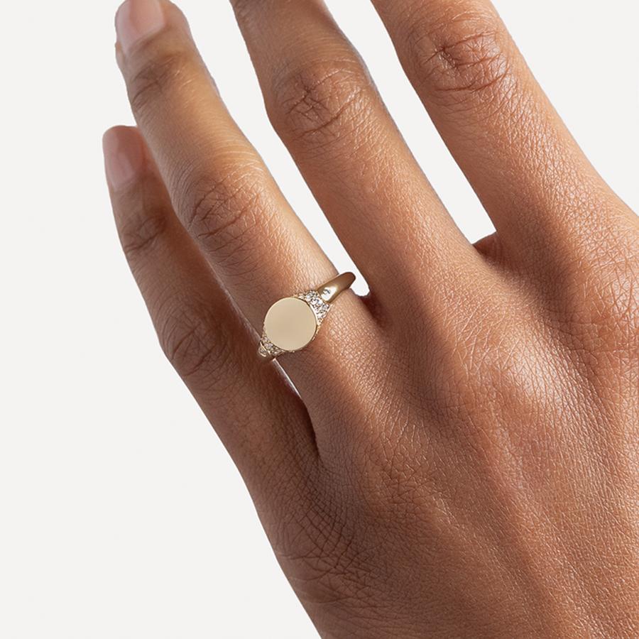 A solid gold signet ring with two white diamond accents on either side and a pave set around the top of the ring and set in yellow gold on a medium-complextion ring finger.