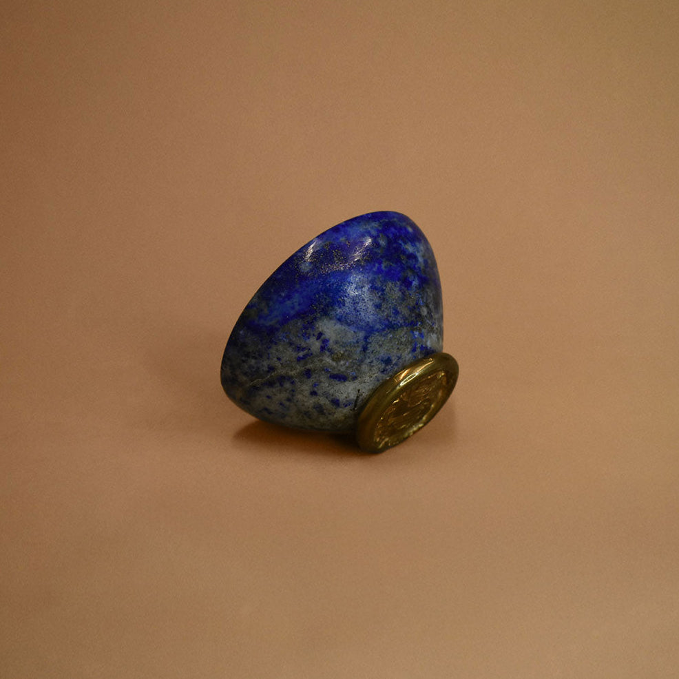 Lapis bowl with a bronze base turned on its side on a beige background