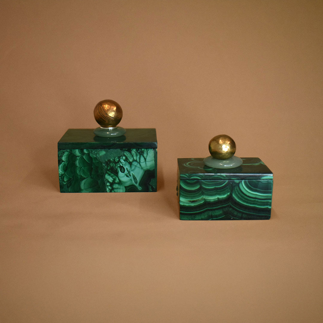 Two malachite boxes with malachite, aventurine, and bronze lids on a beige background
