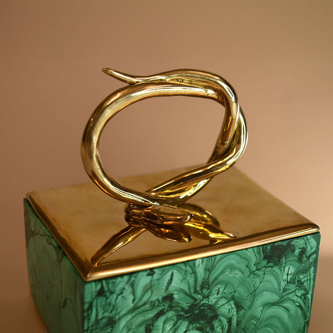 A malachite box with a bronze lid featuring a snake design on a beige background