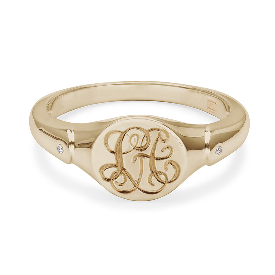 A solid gold signet ring with two white diamond accent stones with interlocking engraving in the center set in yellow gold.