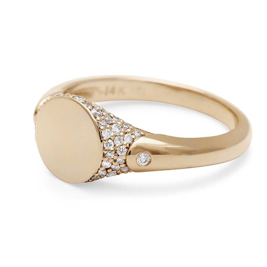 Angled view of a solid gold signet ring with two white diamond accents on either side and a pave set around the top of the ring and set in yellow gold.