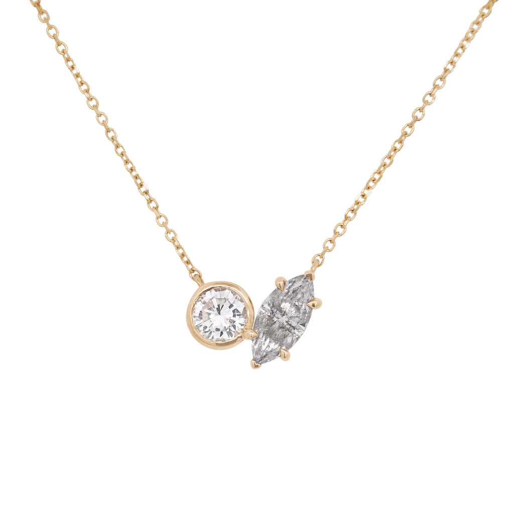 A yellow gold toi et moi necklace featuring a round white diamond and a marquise grey diamond on a white background 