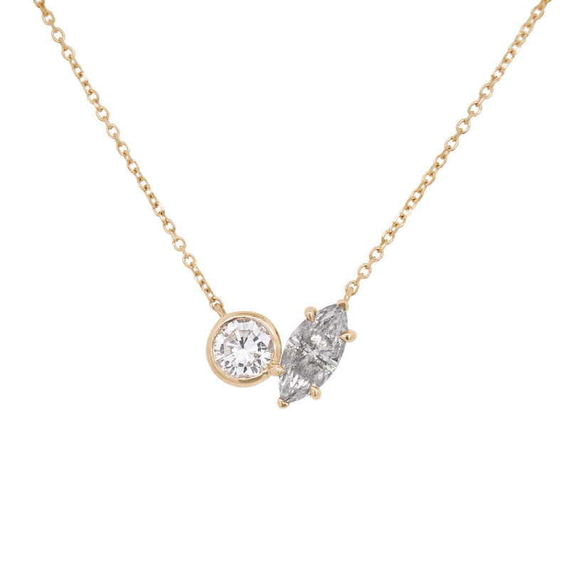 A yellow gold toi et moi necklace featuring a round white diamond and a marquise grey diamond on a white background 