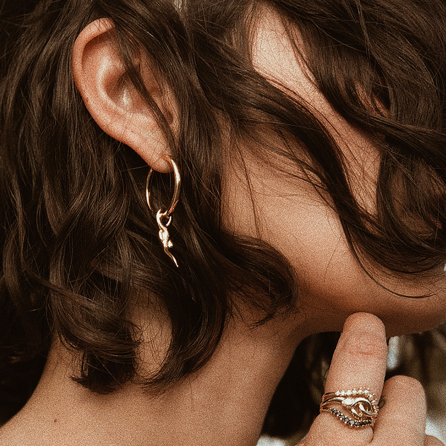 Female wearing - A hoop earring with a serpent charm at the bottom set in yellow gold on a medium complexion model's ear with short brown hair.
