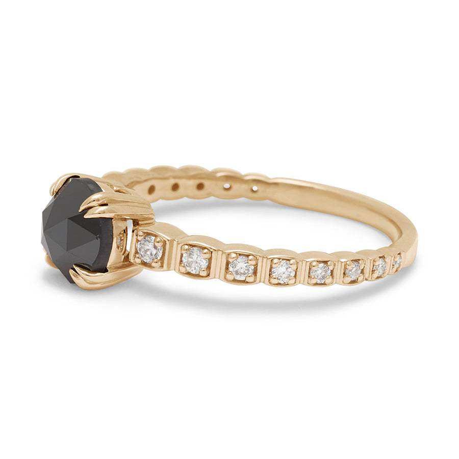 Angled view of a solitaire ring with a round black diamond with white diamond pave around the band set in yellow gold.