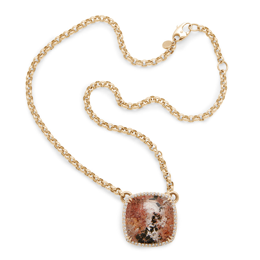 A view of a cushion shaped quartz charm with a desert like scene in a bezel setting with claw prongs and a white diamond halo set in yellow gold on a yellow gold chain with swooped details.