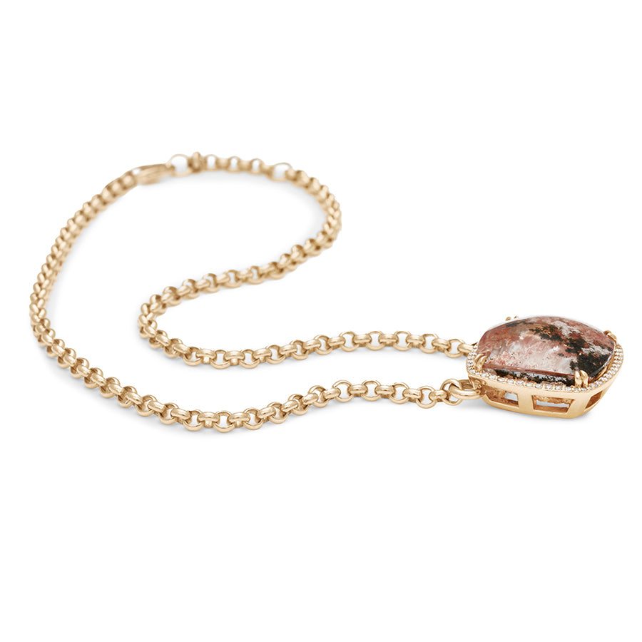 Side view of a cushion shaped quartz charm with a desert like scene in a bezel setting with claw prongs and a white diamond halo set in yellow gold on a yellow gold chain with swooped details.
