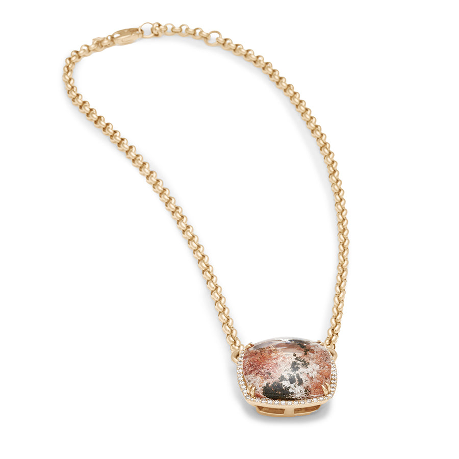 Side view of a cushion shaped quartz charm with a desert like scene in a bezel setting with claw prongs and a white diamond halo set in yellow gold on a yellow gold chain.