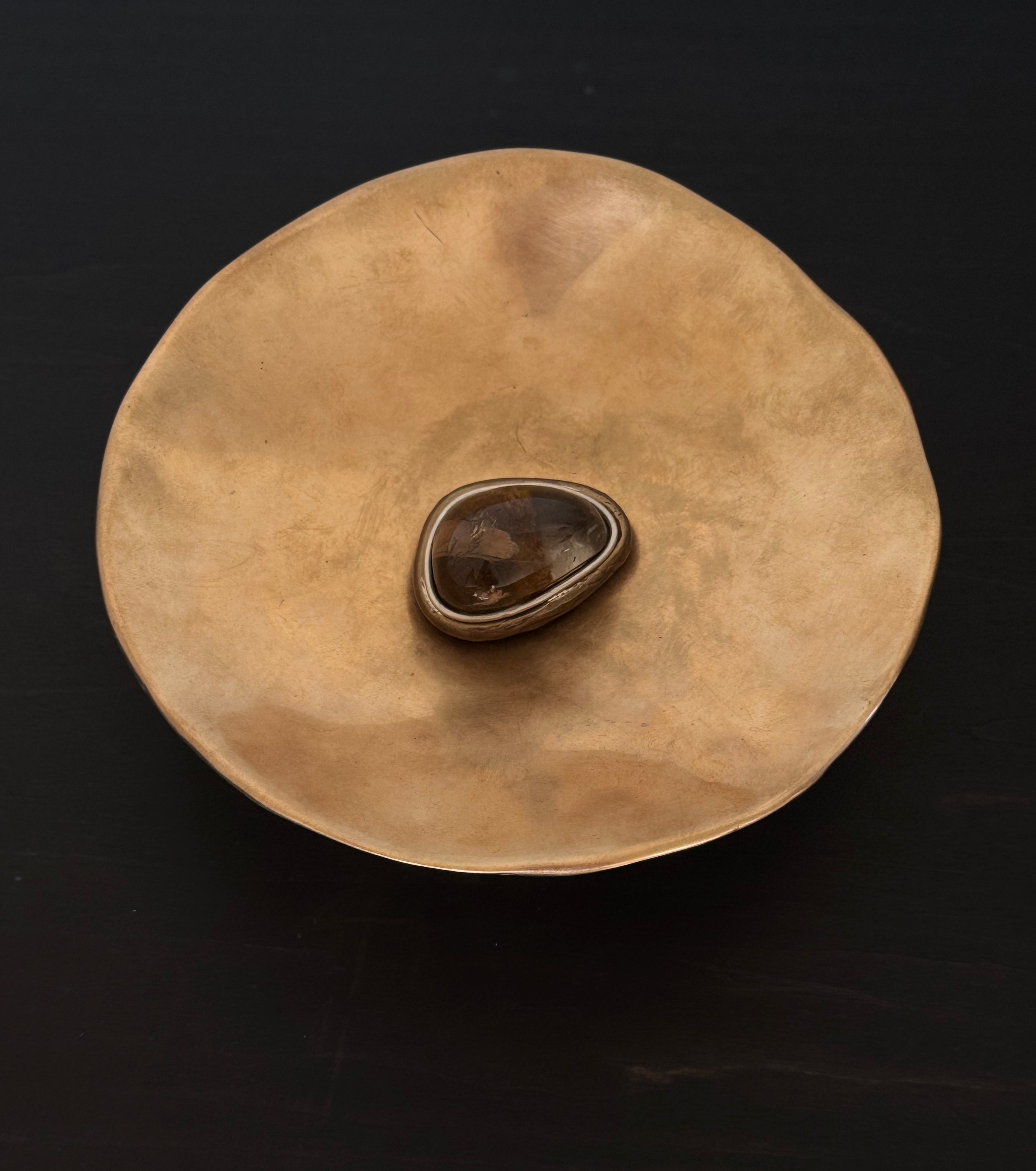 Brass disc bowl with a central brown quartz stone on a black background