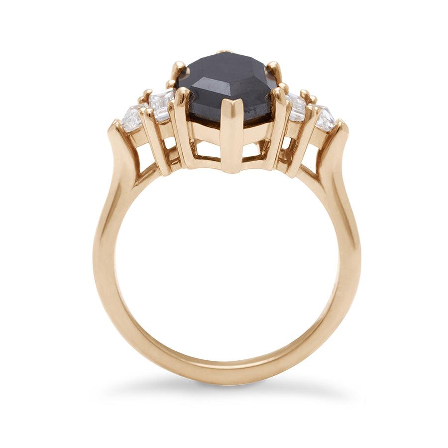 Side view of a ring with a hexagonal shaped black diamond center stone with one baguette white diamond and one white diamond trillion on either side set in yellow gold.