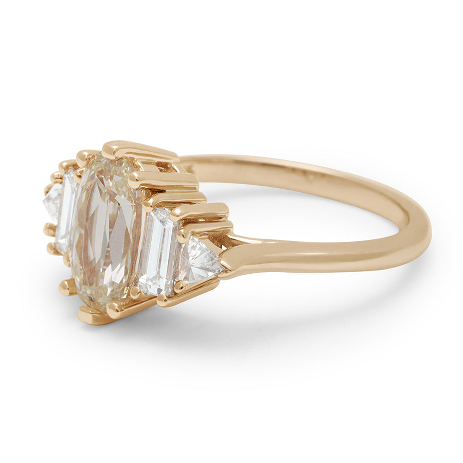Angled view of a ring with a lozenge shaped champagne diamond center stone with one baguette white diamond and one white diamond trillion on either side set in yellow gold.
