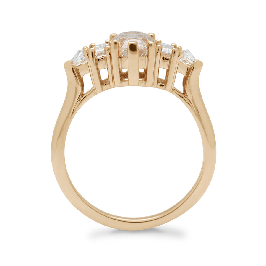 Side view of a ring with a lozenge shaped champagne diamond center stone with one baguette white diamond and one white diamond trillion on either side set in yellow gold.