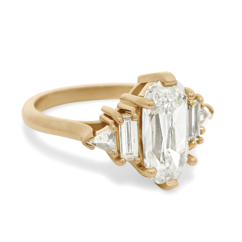 Side profile of a gold five stone ring with a large elongated cushion diamond center stone and smaller baguette and trillion diamond side stones on a white background