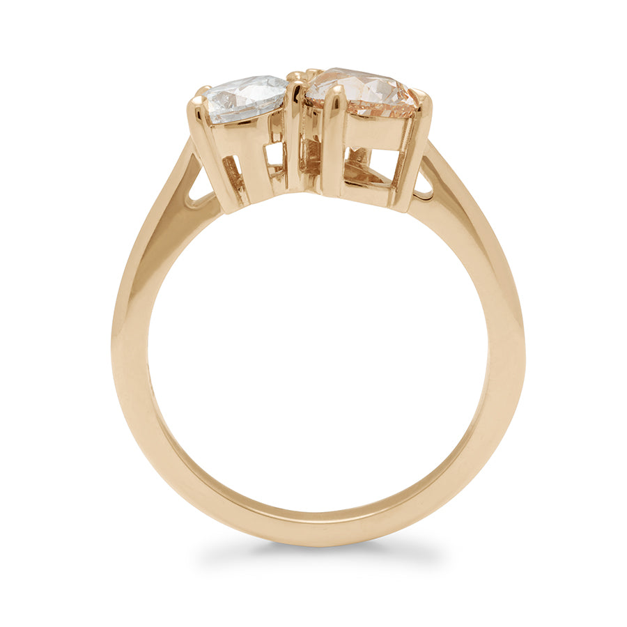 Side view of a two diamond ring with a pear champagne diamond set next to a round white diamond set in yellow gold.