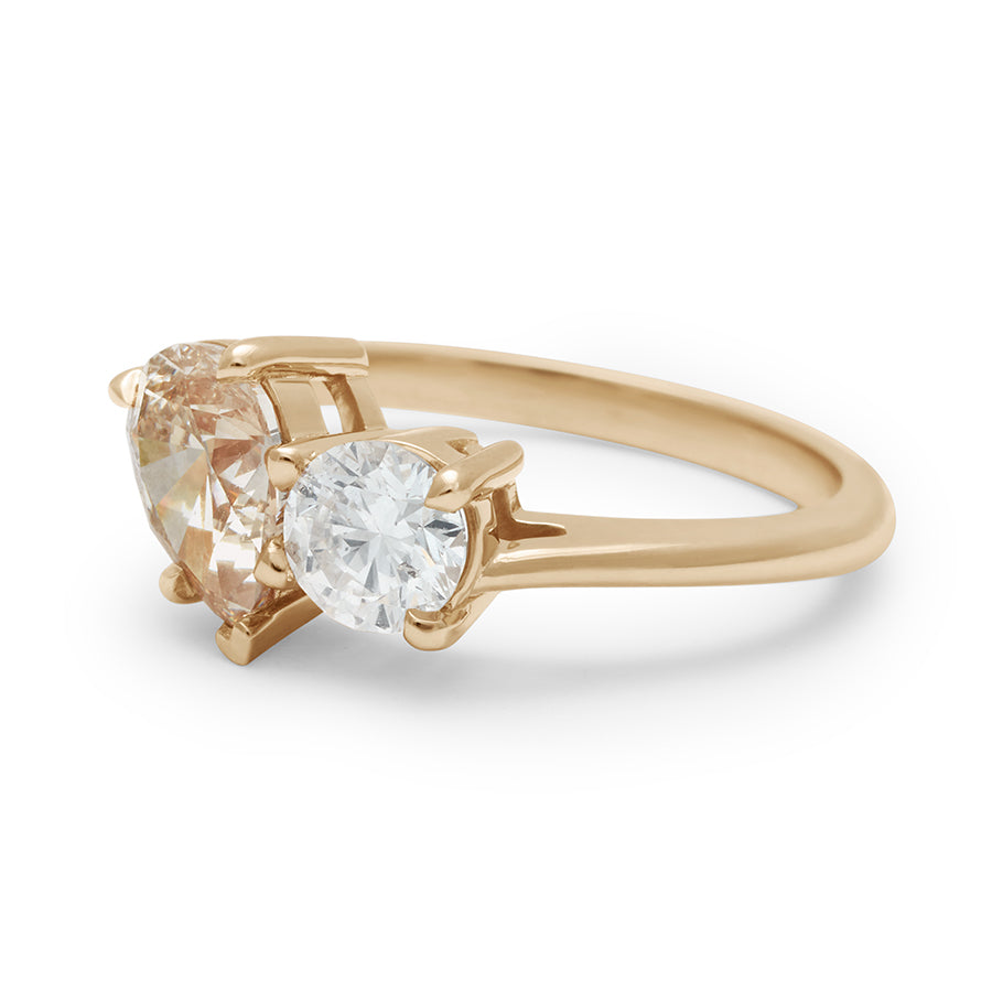 Angled view of an upside down view of a two diamond ring with a pear champagne diamond set next to a round white diamond set in yellow gold.