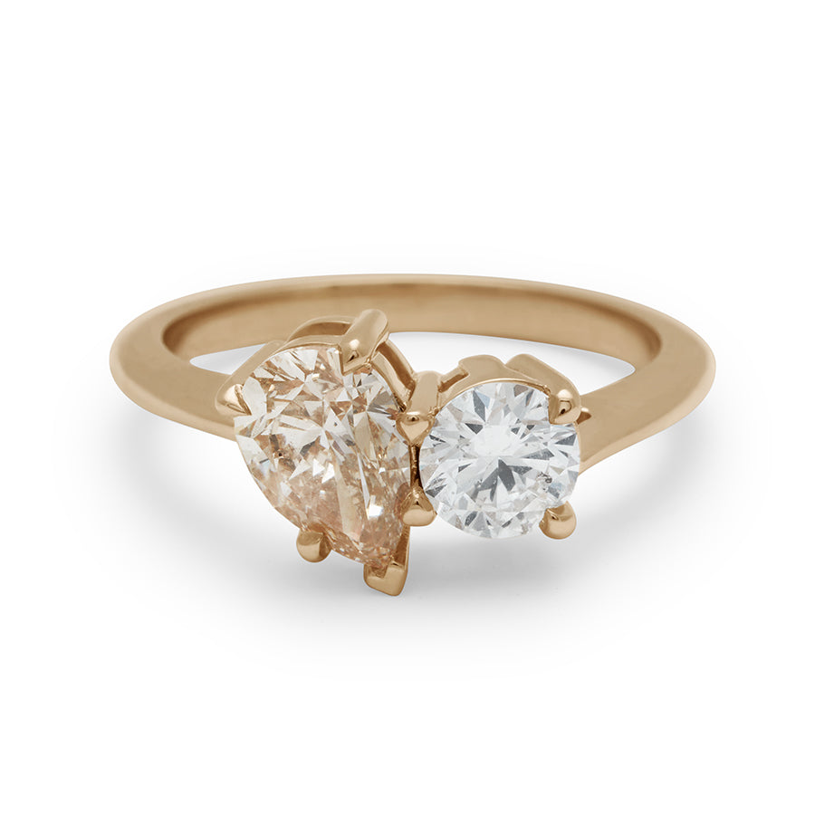 An upside down view of a two diamond ring with a pear champagne diamond set next to a round white diamond set in yellow gold.