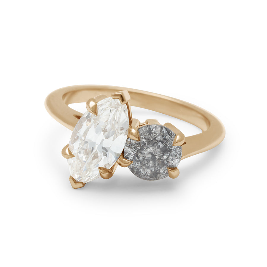 A rotated view of a two diamond ring with a marquise white diamond set next to a round grey diamond set in yellow gold.