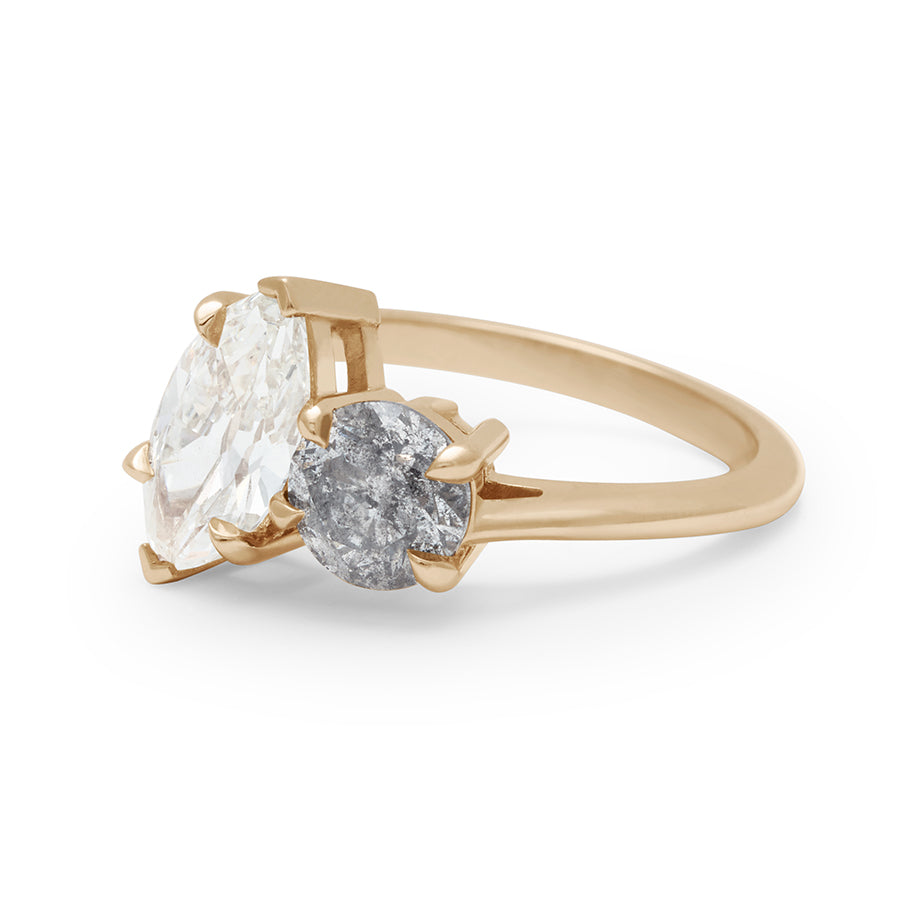 Angled view of a two diamond ring with a marquise white diamond set next to a round grey diamond set in yellow gold.