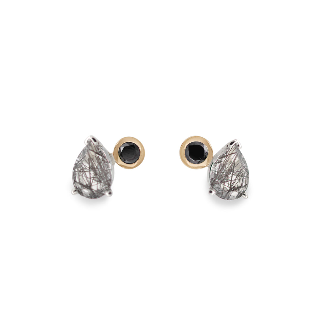 A pair of stud earrings featuring pear shaped black rutile quartz and round black diamonds set in sterling silver and yellow gold on a white background.