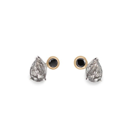 A pair of stud earrings featuring pear shaped black rutile quartz and round black diamonds set in sterling silver and yellow gold on a white background.