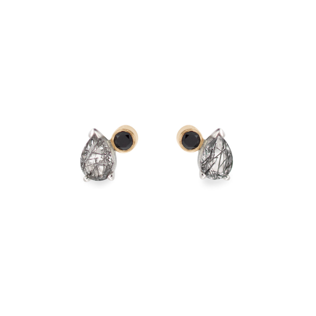 A pair of stud earrings featuring pear shaped black rutile quartz and round black diamonds set in yellow gold and sterling silver on a white background.