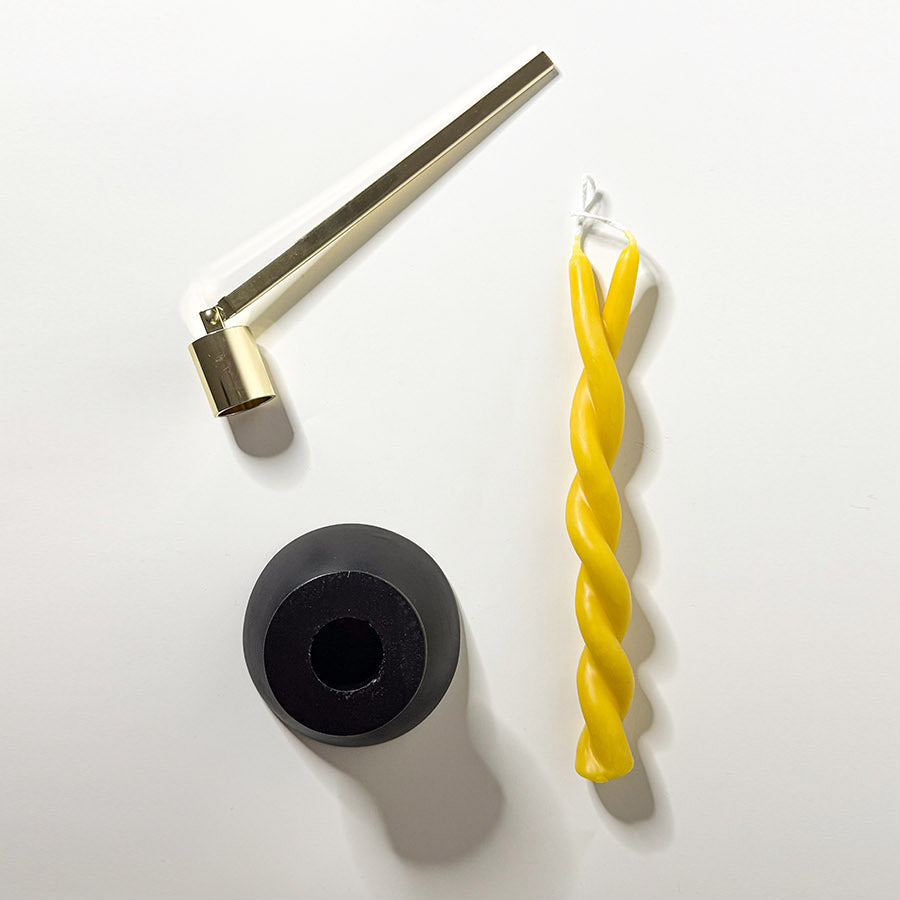 A black candle holder with a yellow twisted candle and a brass candle snuffer next to it.