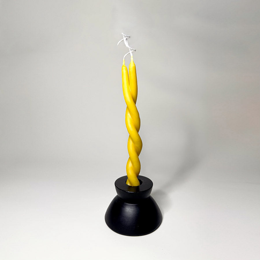 A black candle holder holding a yellow twisted candle to symbolize a twin flame.