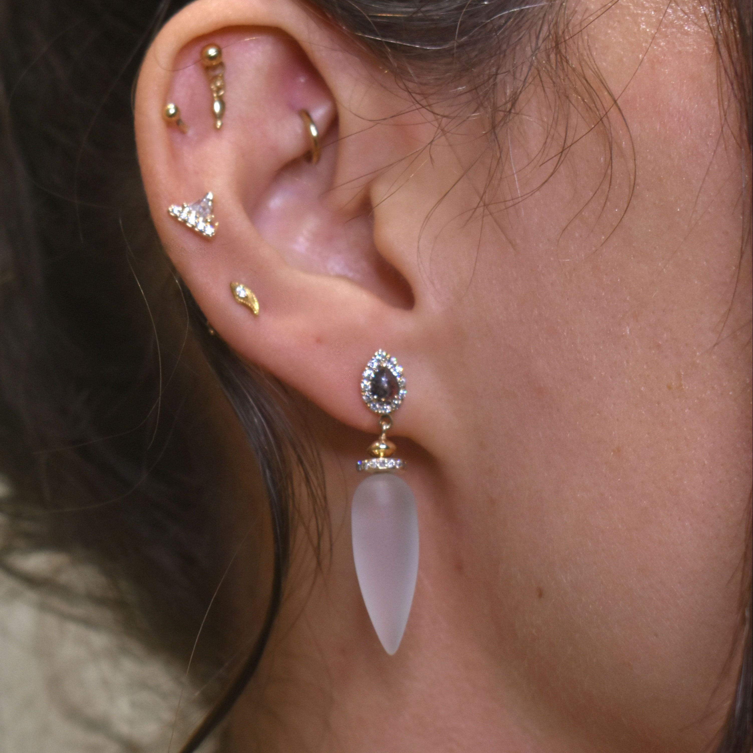 A close-up of a frosted quartz drop earring featuring grey and white diamonds set in yellow gold worn by a person.