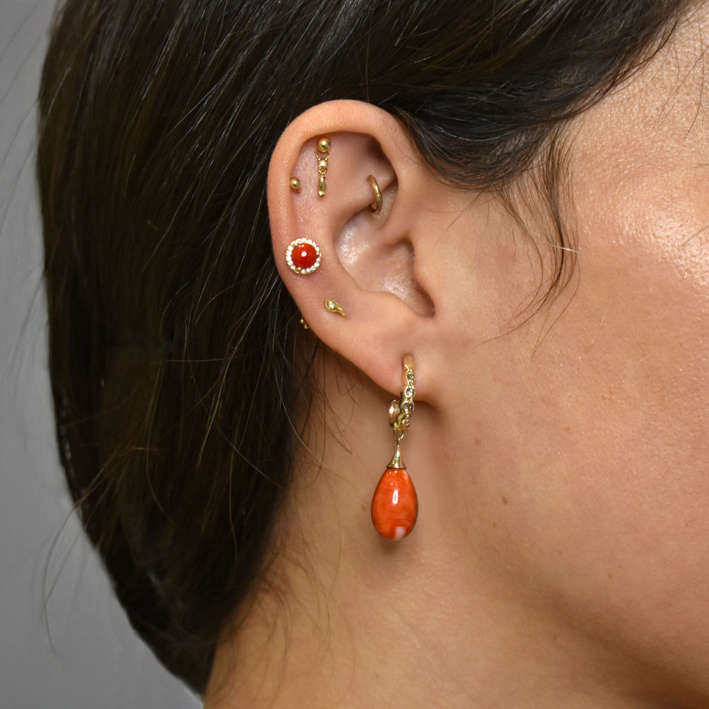 A photo of an ear stack featuring coral drop earrings set in yellow gold, and other gold studs and a coral earring with a diamond halo. 