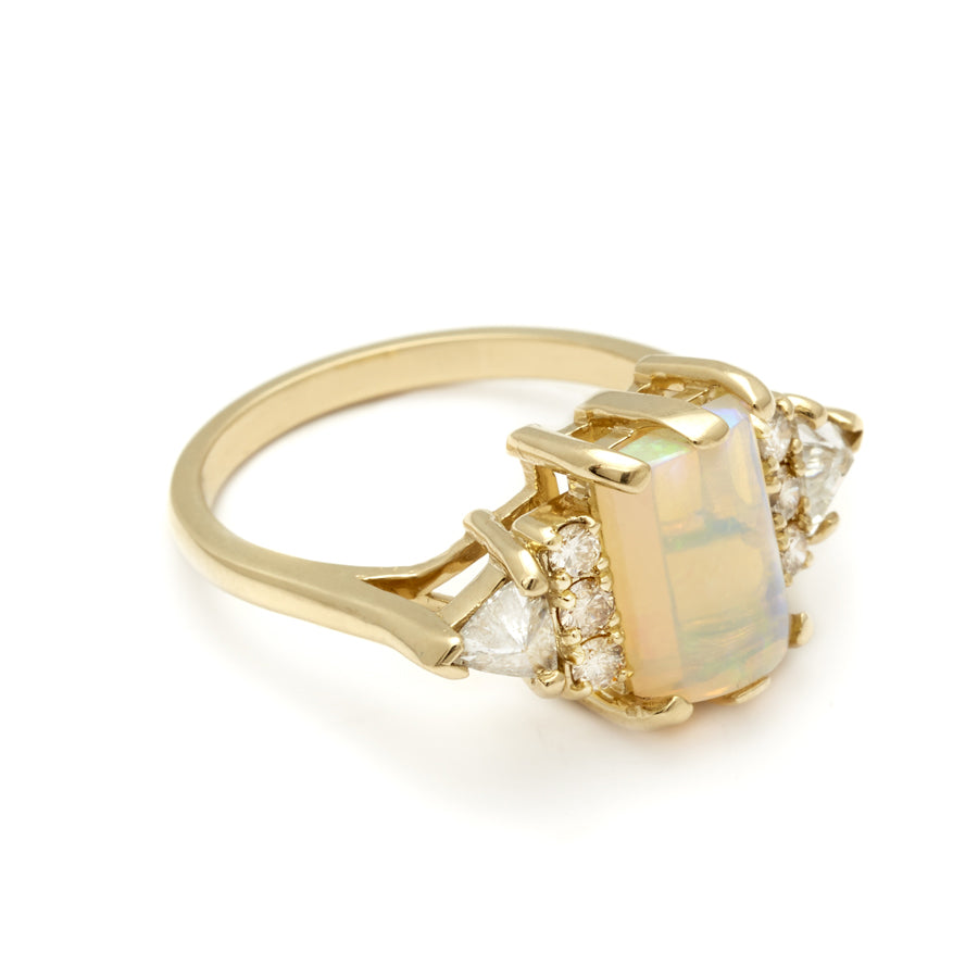Angled view of an emerald shape opal cabochon center stone ring with three round white diamonds on either and two white diamond trillions on the outer edges of each side set in yellow gold.