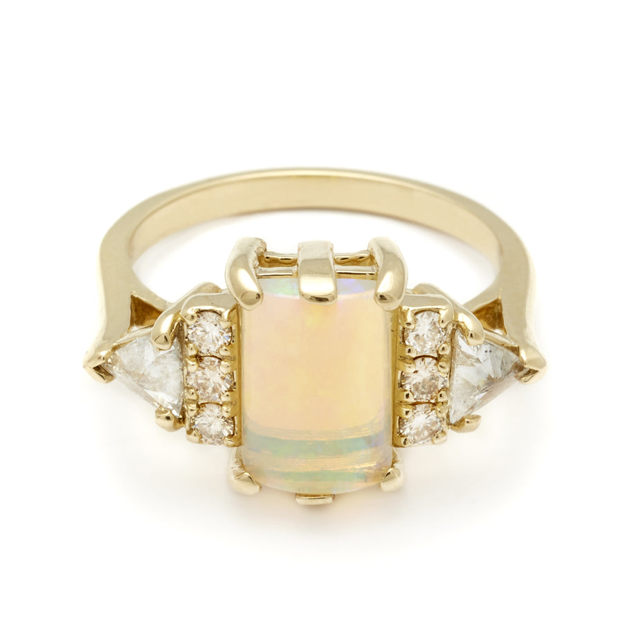 An emerald shape opal cabochon center stone ring with three round white diamonds on either and two white diamond trillions on the outer edges of each side set in yellow gold.