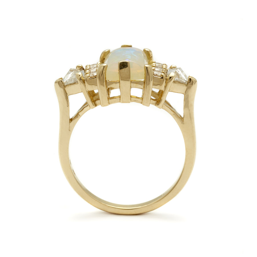 Side view of an emerald shape opal cabochon center stone ring with three round white diamonds on either and two white diamond trillions on the outer edges of each side set in yellow gold.